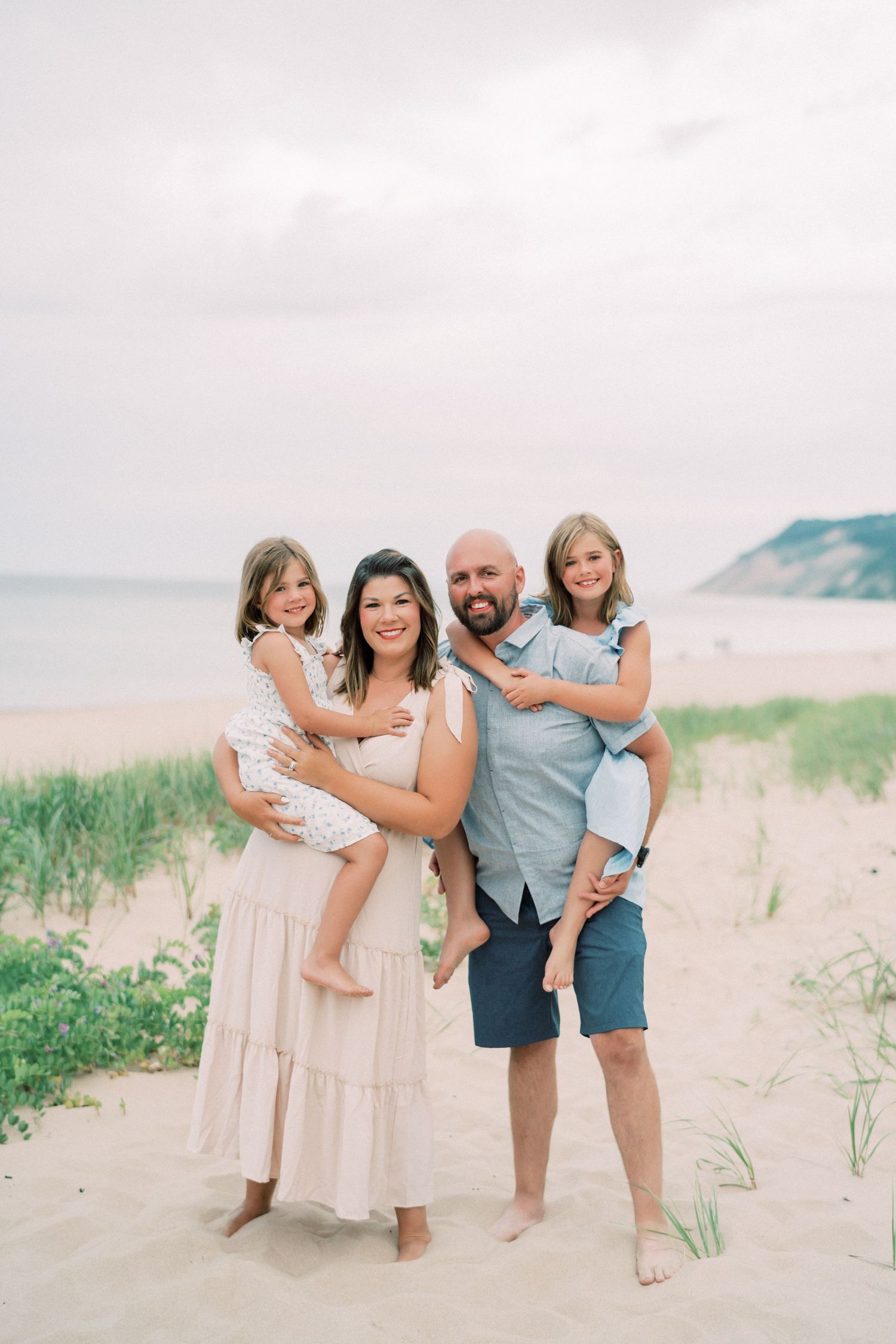 Family group enjoying a sunny day together at a scenic beach with sand dunes and coastal vegetation.