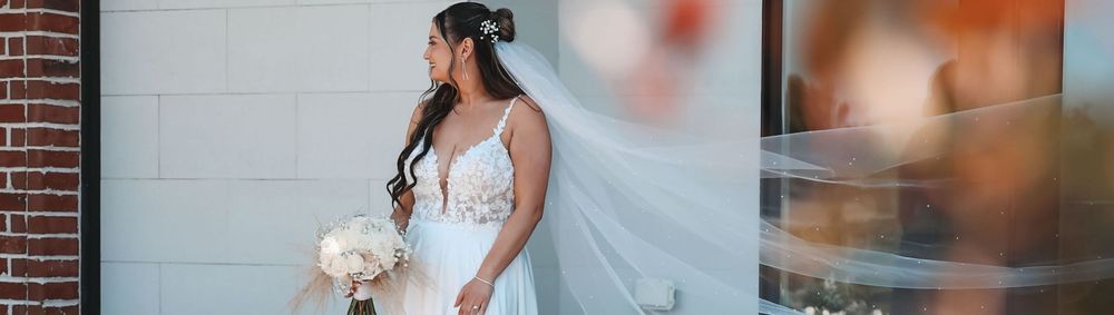 Bride in beautiful white lace wedding gown and veil poses against brick wall at golden hour.