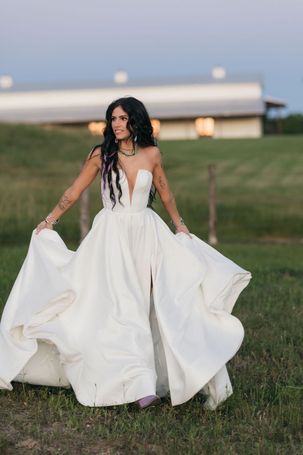 A bride twirls her elegant white ball gown in a countryside setting with a barn in the background.