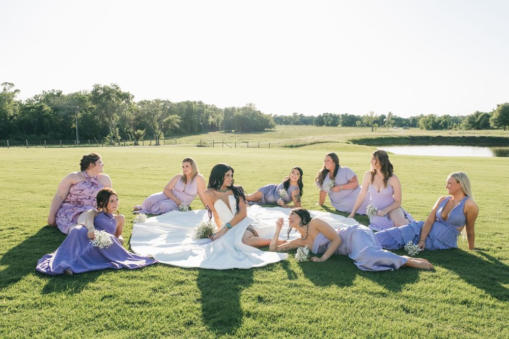 Wedding party lounging on grass during outdoor photo session with white and purple color scheme.