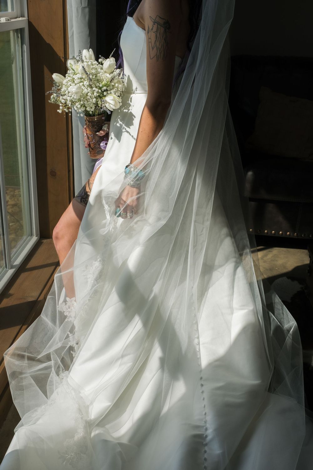 Elegant white wedding dress with flowing tulle and a simple bouquet captured in natural window light.