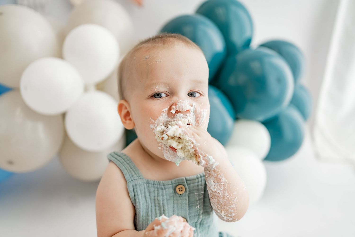 A young child in teal and white party decorations enjoys a white frosted cake with colorful sprinkles.