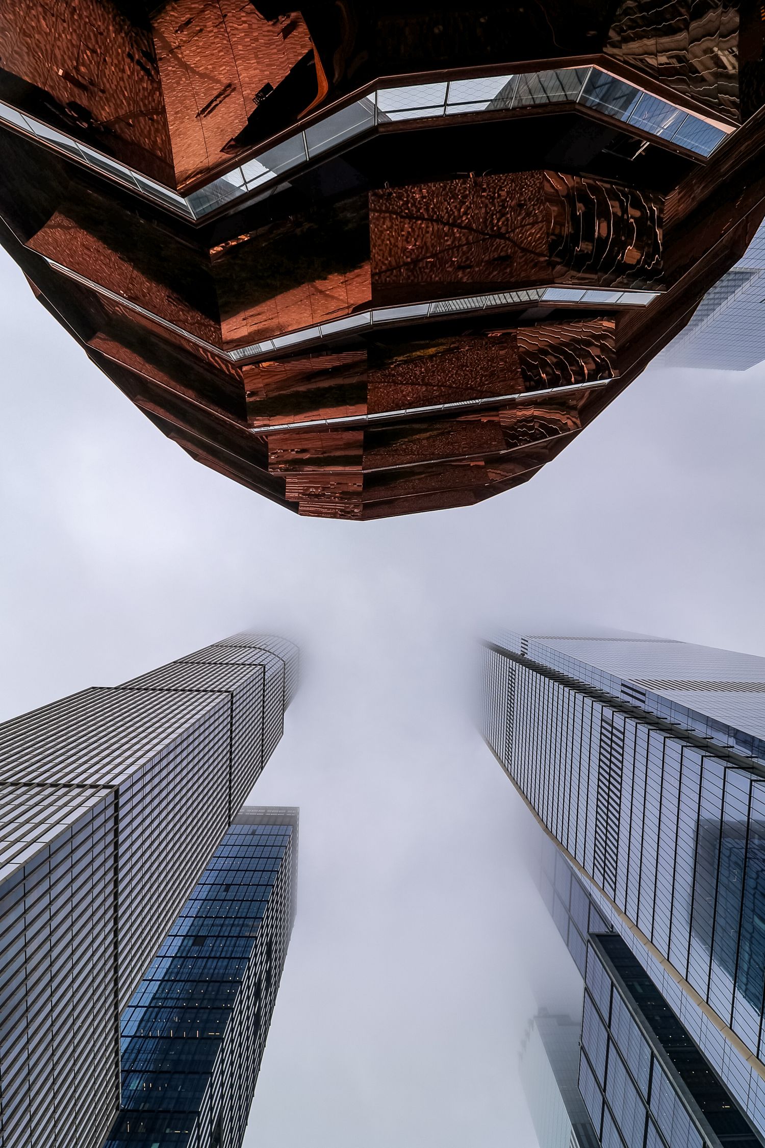 Looking up at modern glass skyscrapers in an urban setting with a reflective architectural feature overhead forming a spiral.