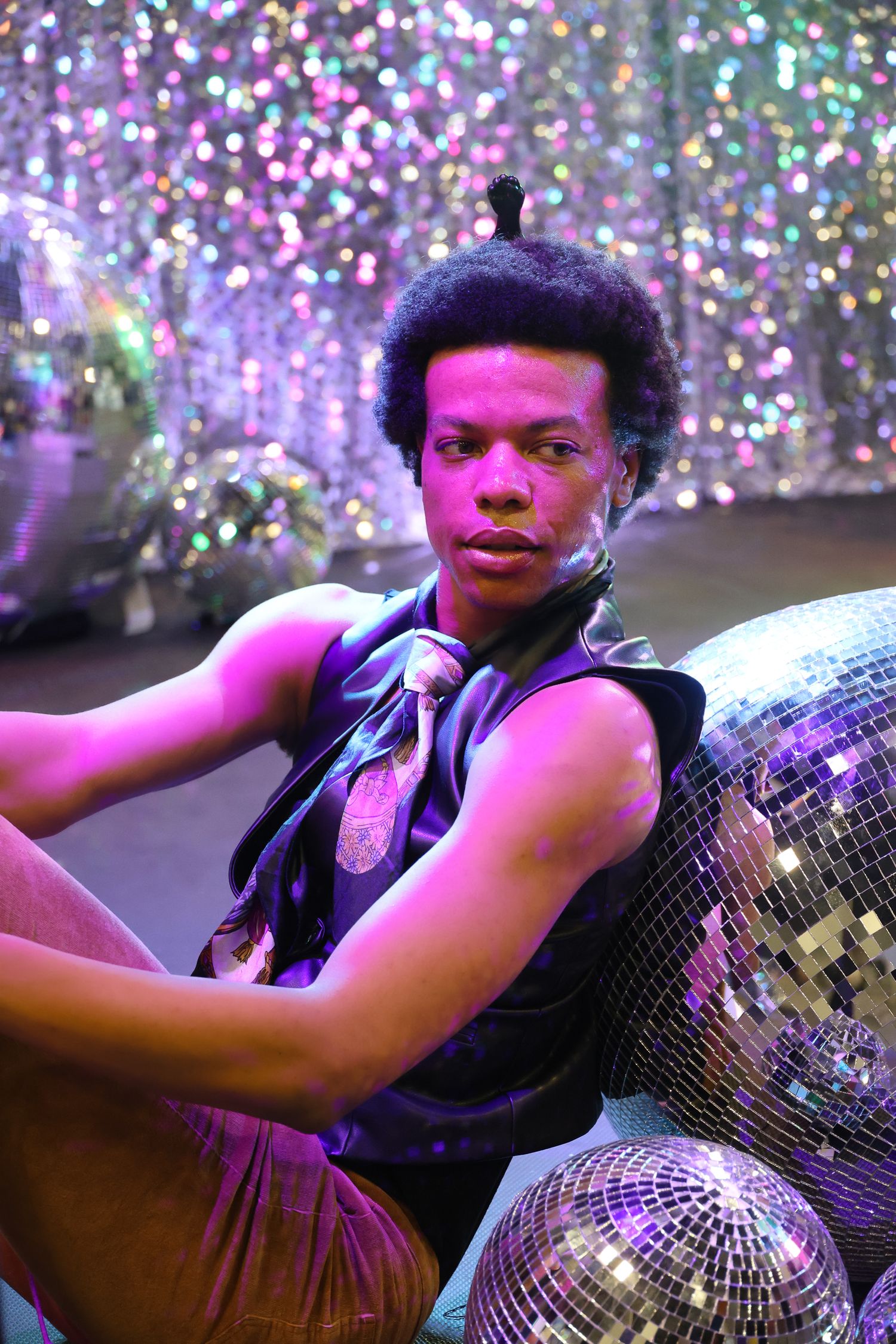 Person in black vest poses with disco balls surrounded by sparkly pink and purple lighting effects.