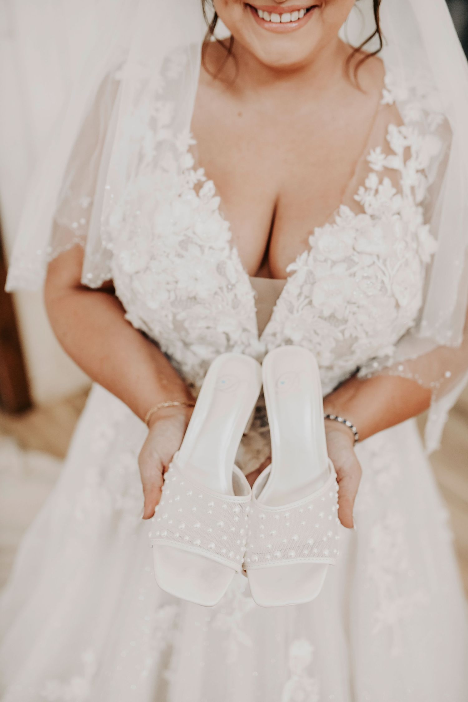 Bride holding pearl-embellished wedding shoes with soft natural light