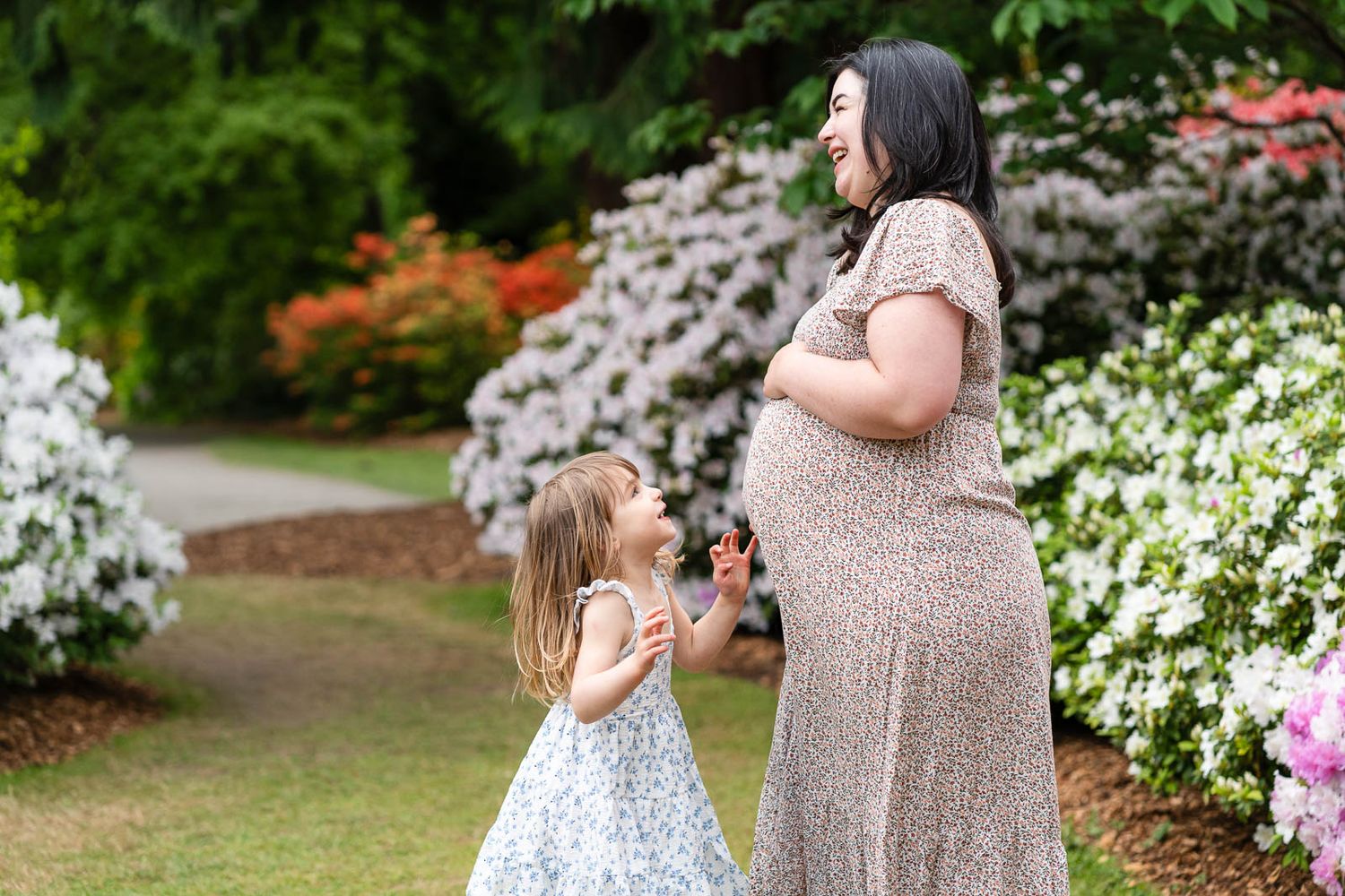 Mom pregnant and smiling while daughter looks on.