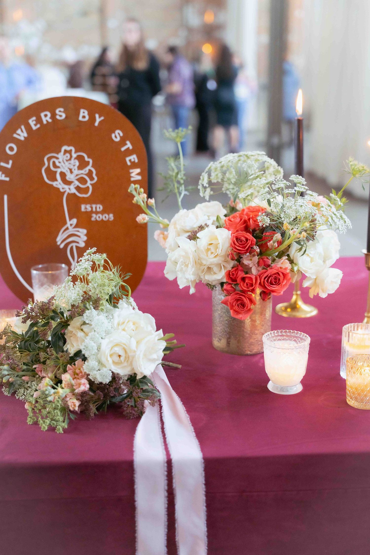 Elegant floral centerpieces with roses on a burgundy tablecloth next to a rustic wooden branded sign. At Fairlie, Chicago