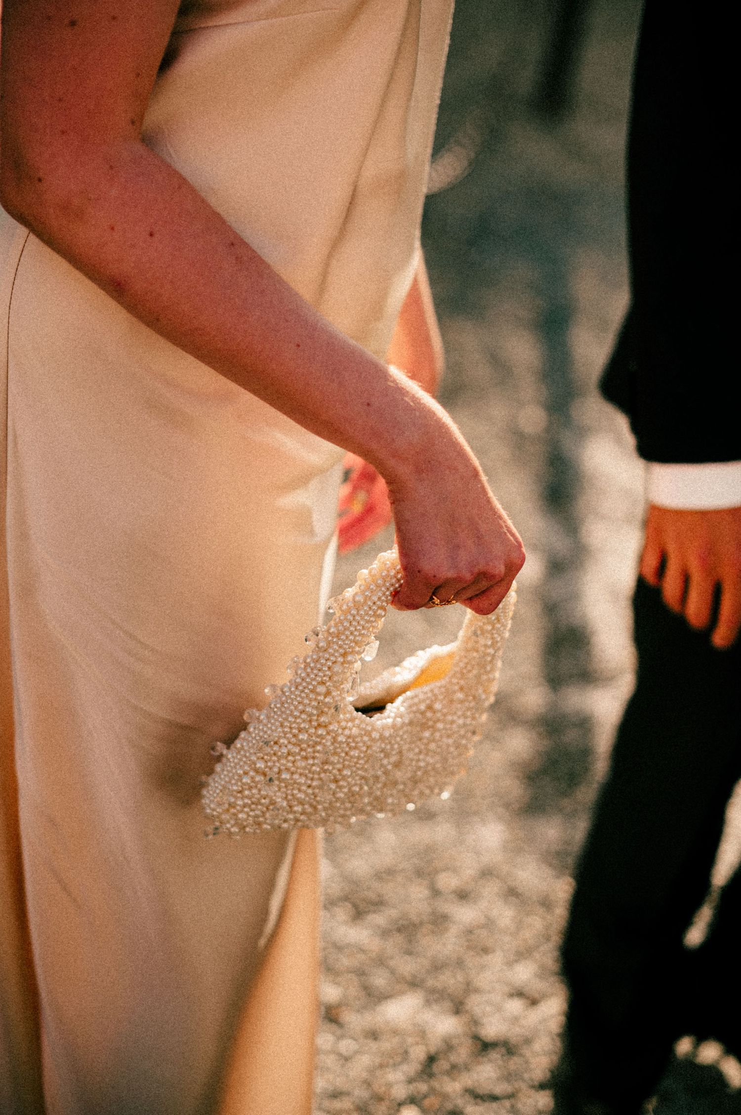 A close-up shot of someone holding a beaded wedding purse against a cream-colored dress.
