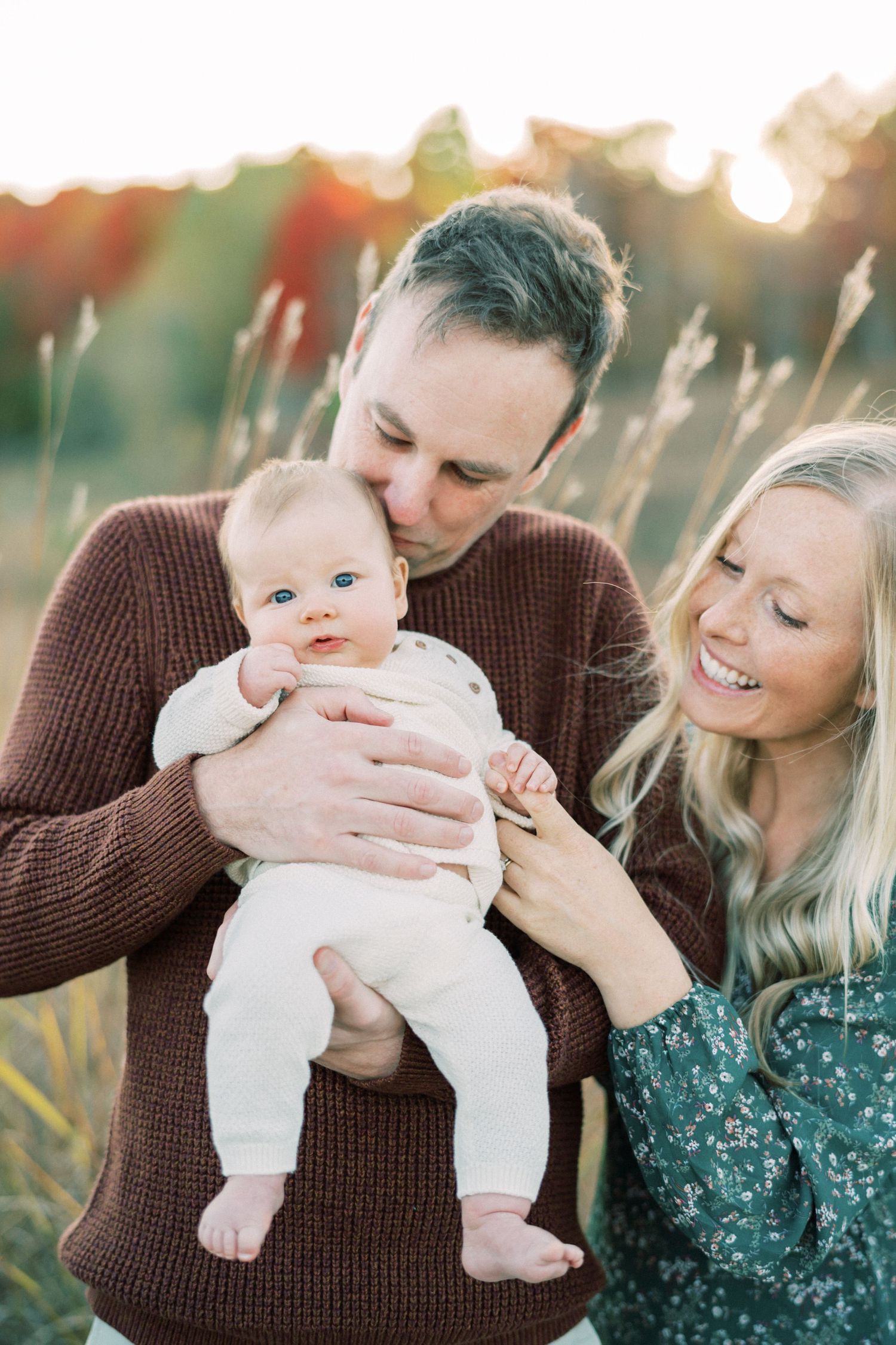 Beautiful family moment captured outdoors at sunset with a small baby and parents.
