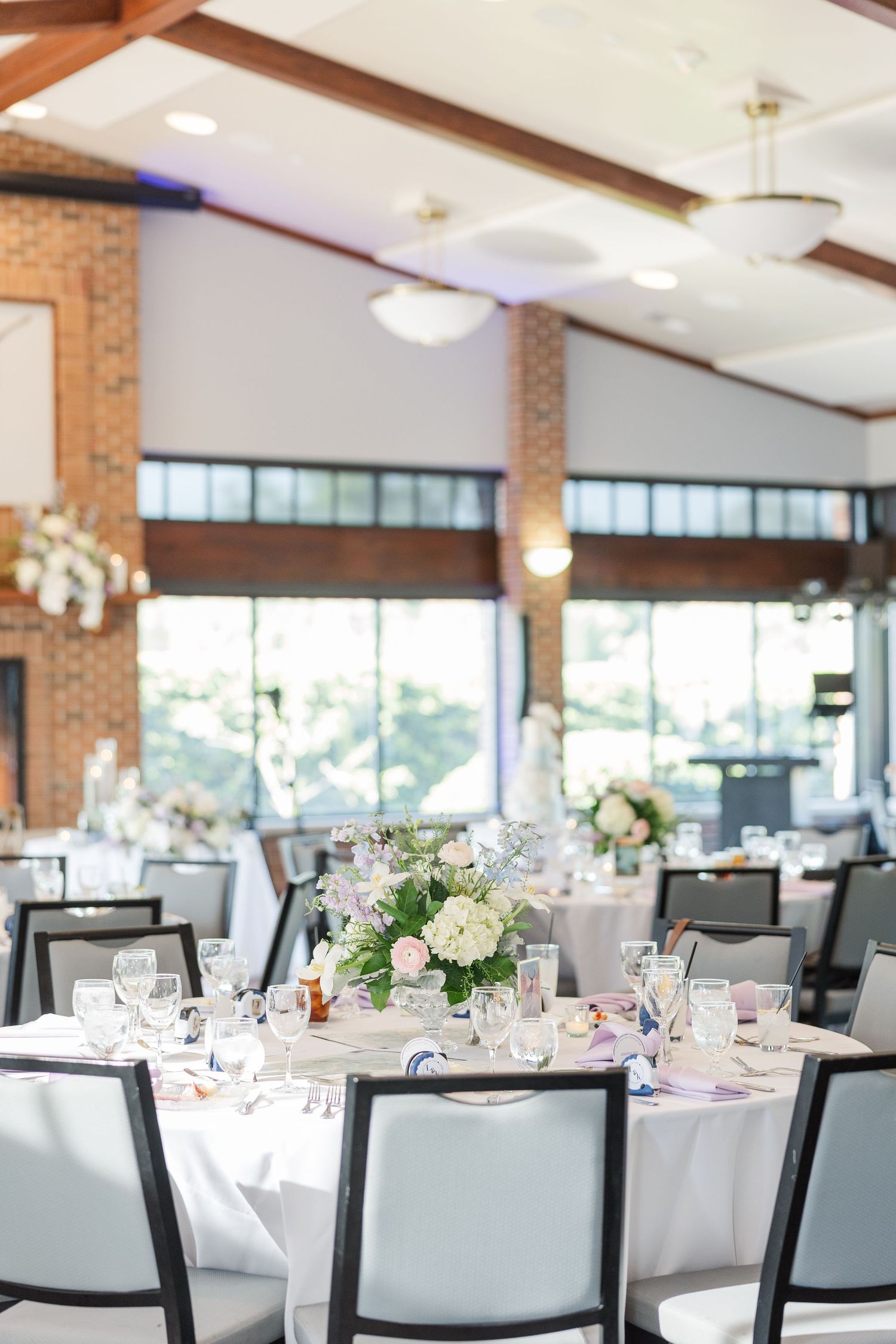 Elegant wedding reception venue with round tables, white linens, and floral centerpieces in a room with exposed brick walls.