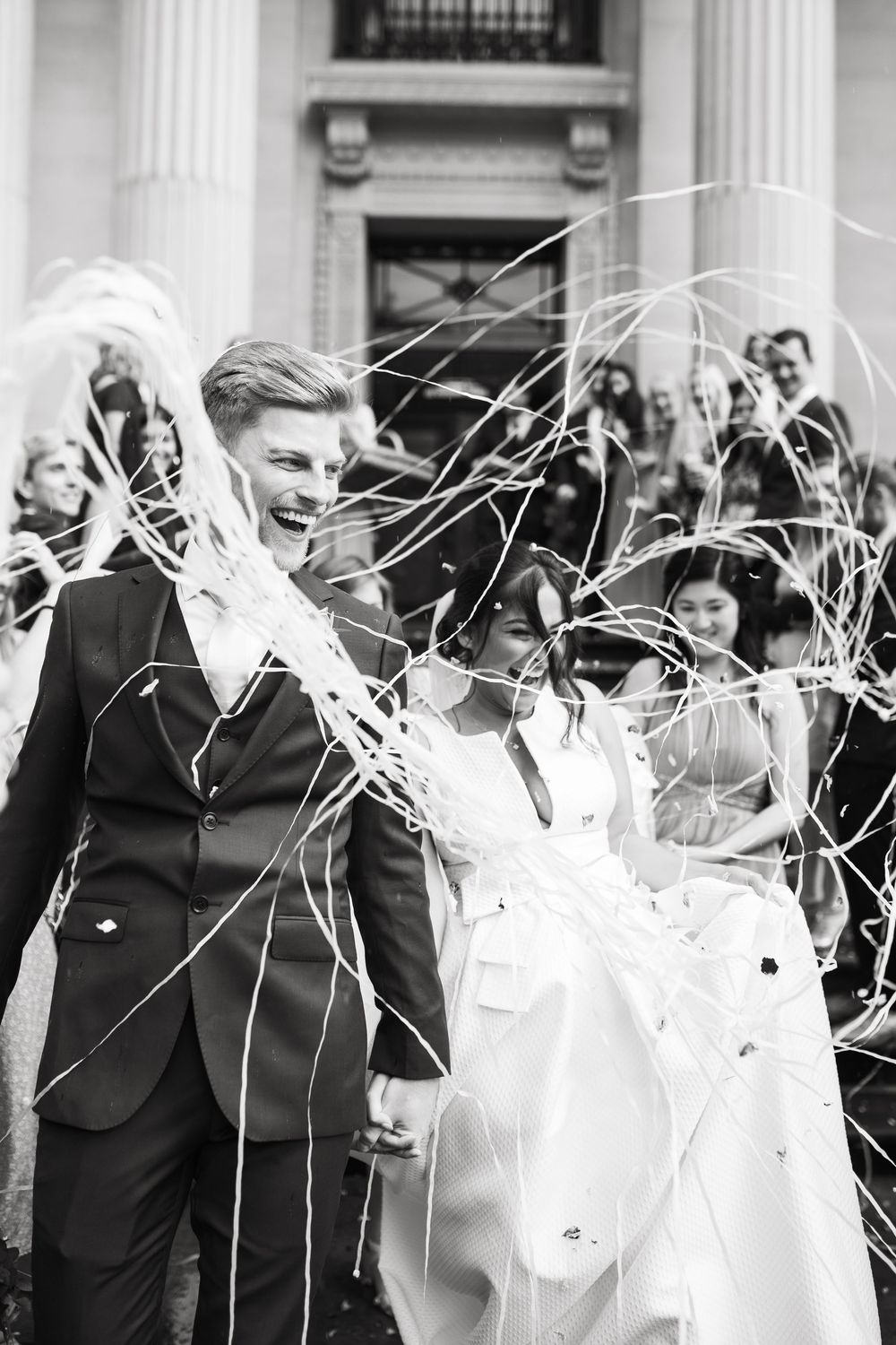 Black and white photo of couple being showered with streamers on historic building steps.