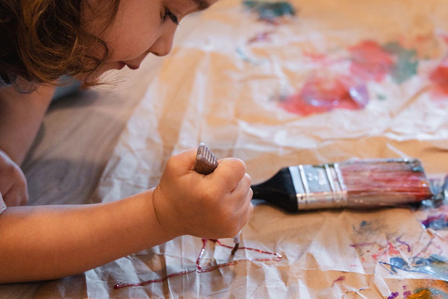 A child's hand uses art supplies on paper during a creative painting session with watercolors and brushes.