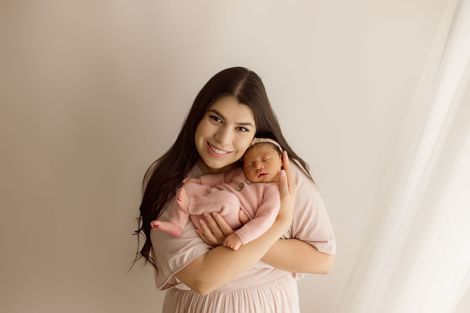 Newborn baby sleeps peacefully while being cradled in a light pink setting.