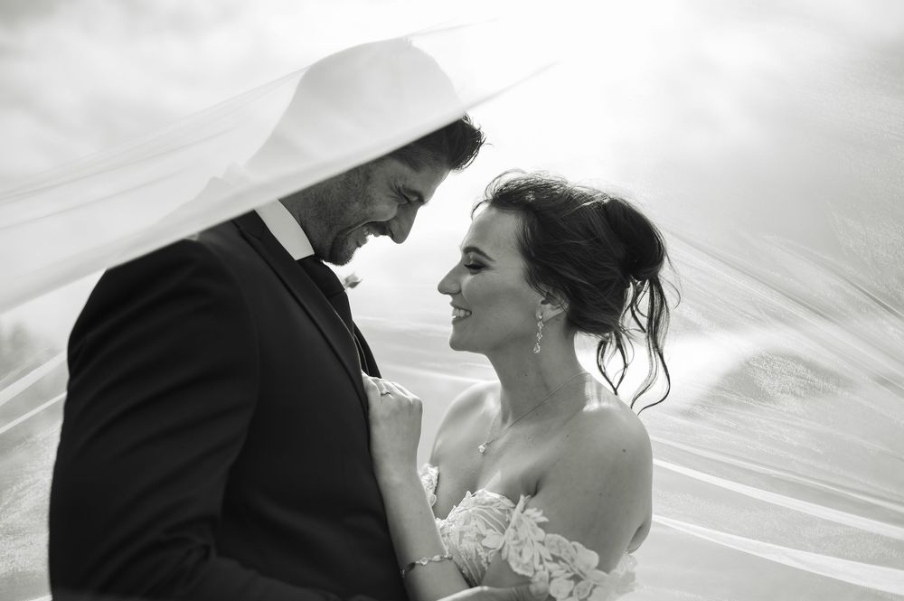 A tender black and white wedding portrait with flowing veil creating romantic atmosphere.