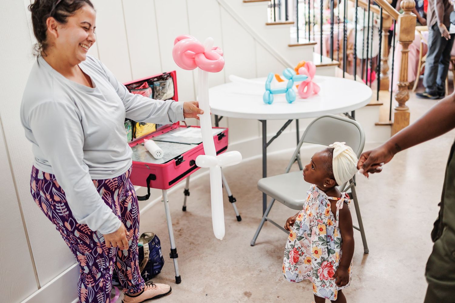 A balloon artist hands a small child a creation at a first birthday party