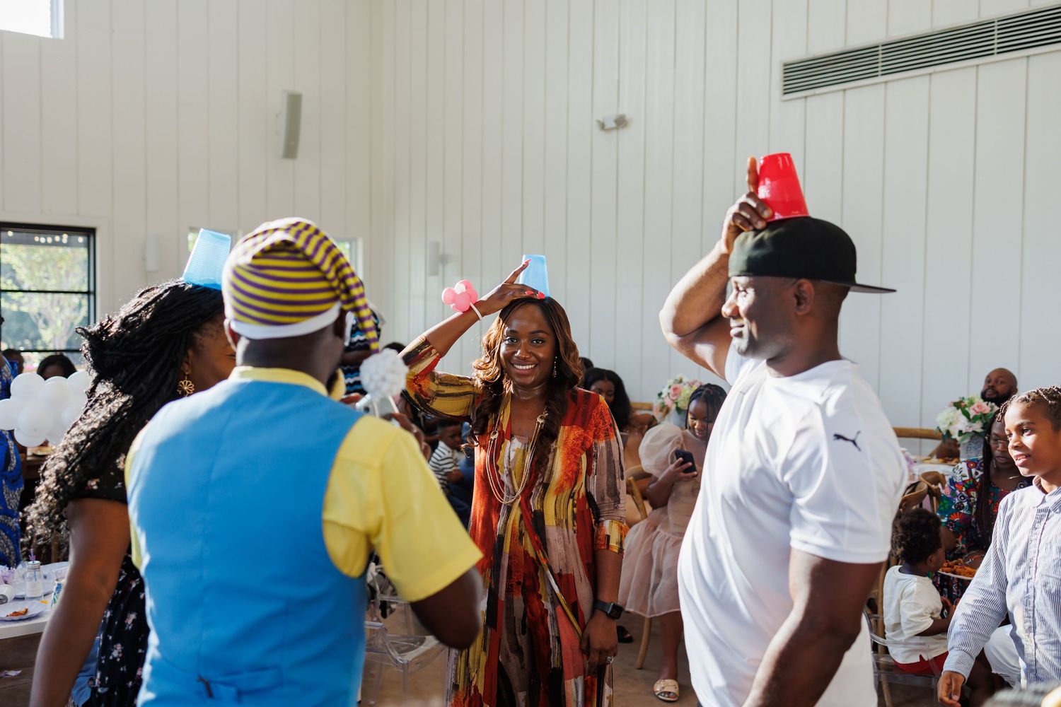 Adults play a game with cups on their heads at a first birthday party at Bella Cavalli