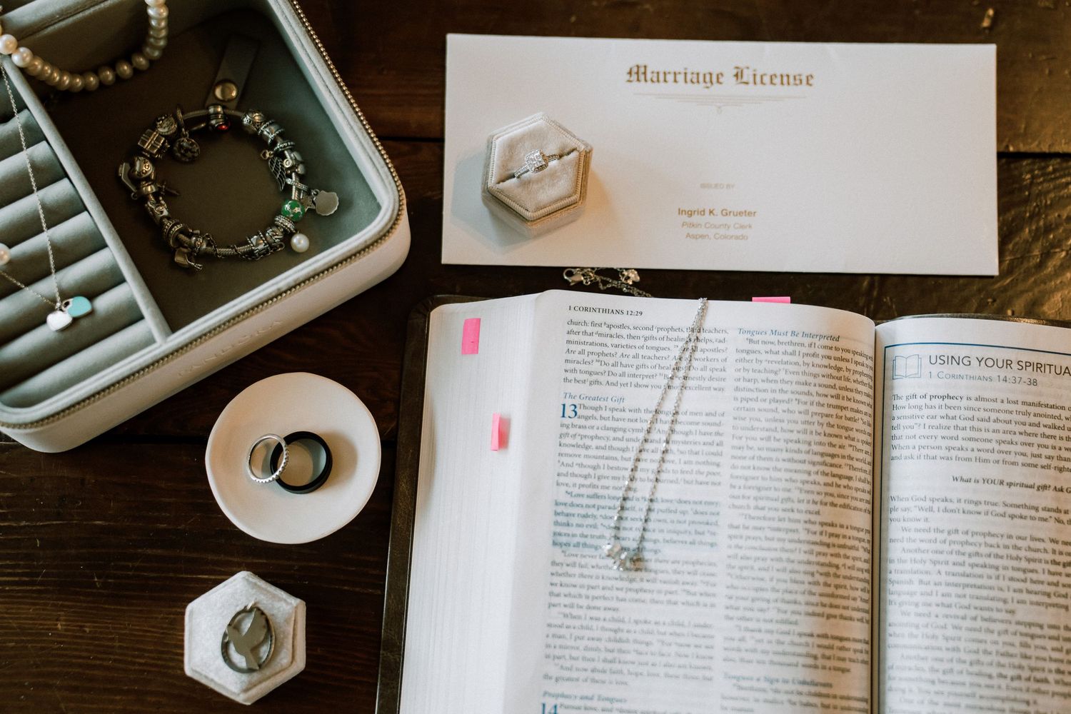 An open book with wedding rings, a hexagonal ring box, and vintage typewriter on a dark wooden desk.