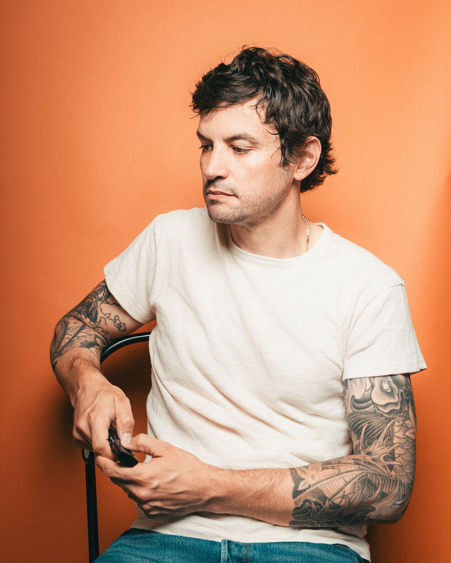 Black and white portrait of Nick Streeter in white t-shirt with visible arm tattoos sitting against neutral background.