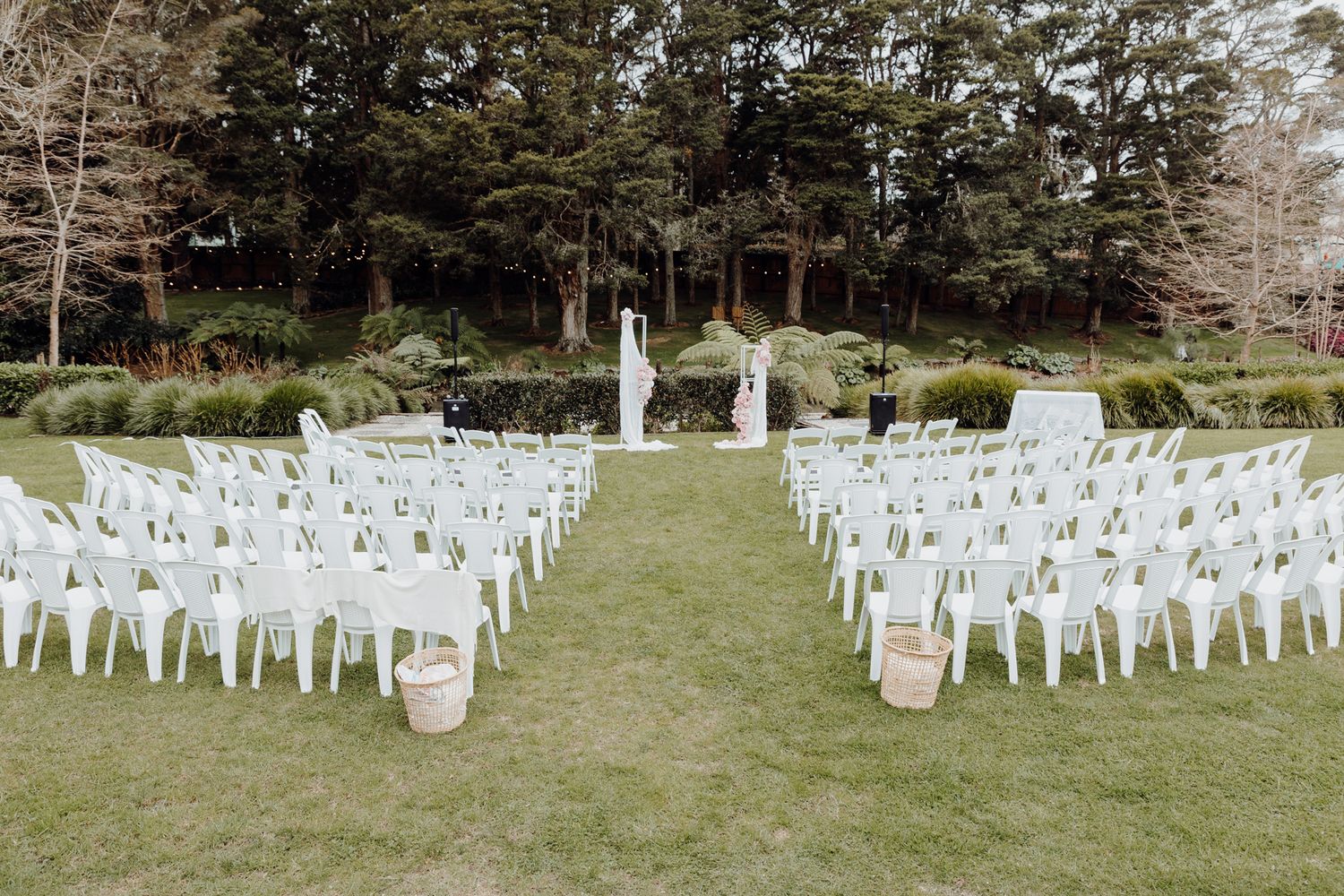 Outdoor wedding ceremony setup with rows of white chairs and an aisle leading to a floral arch.