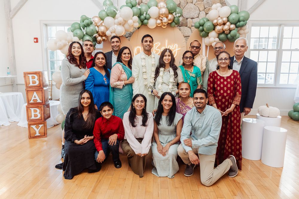 Large group photo of family and friends at a baby shower with balloon decorations and 'BABY' blocks.