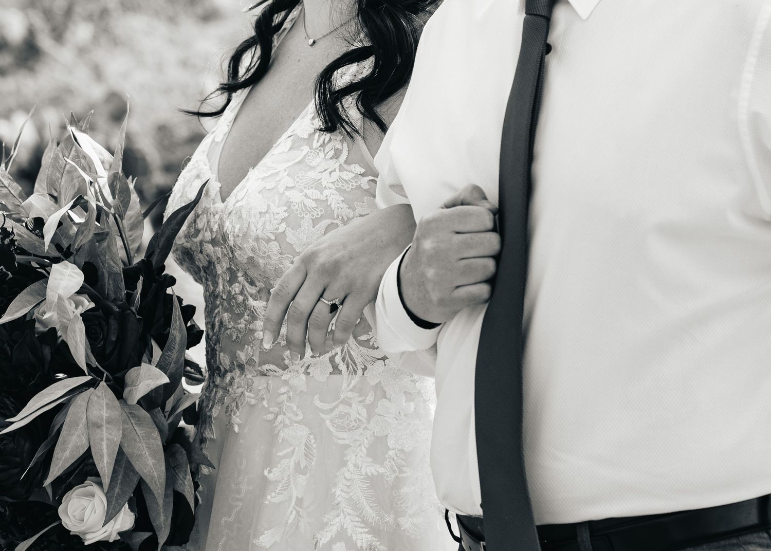 Black and white close-up of couple in wedding attire showing intricate lace dress details and floral bouquet.