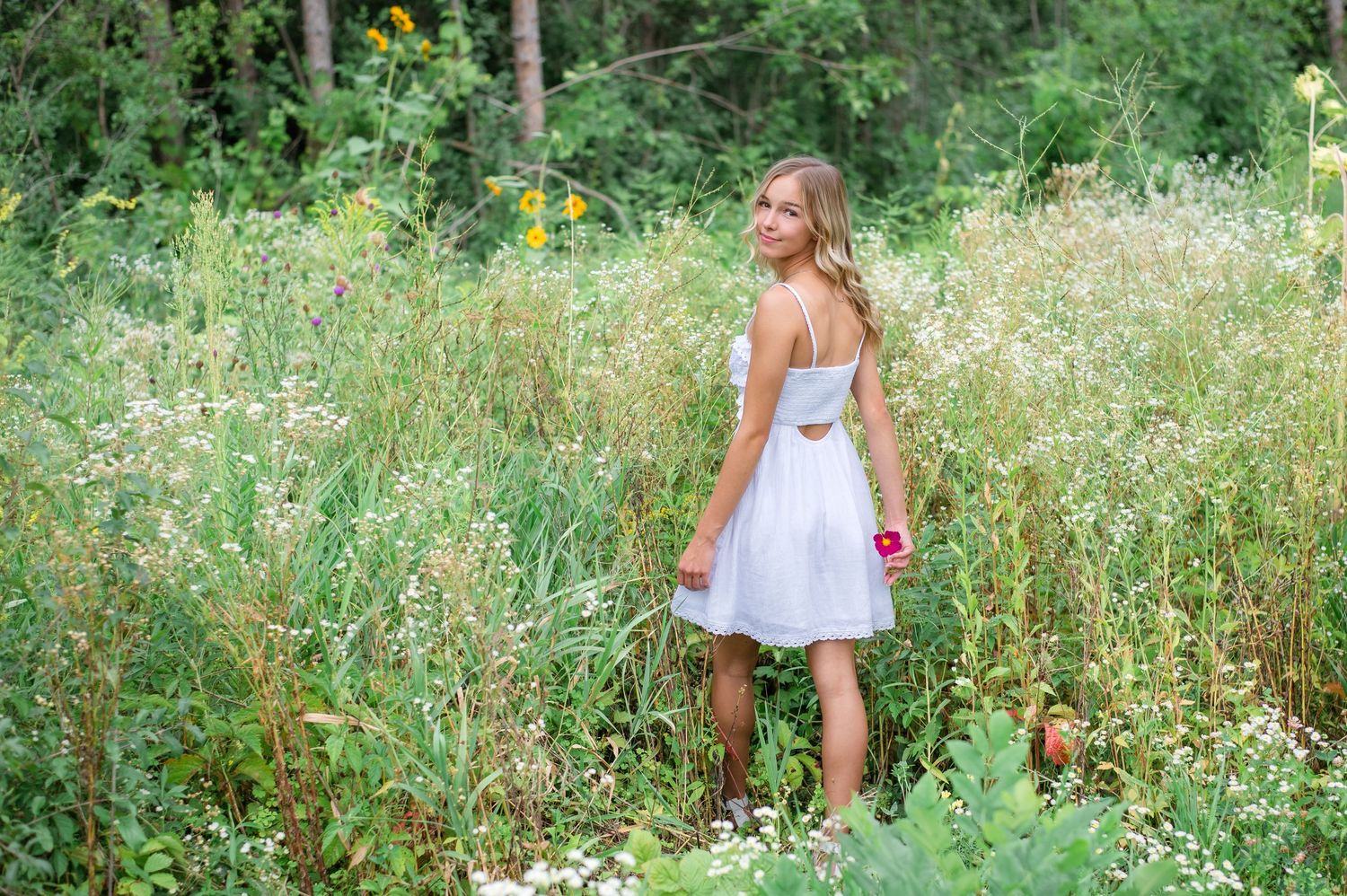 A person in a white sundress stands in a wildflower meadow during summer.