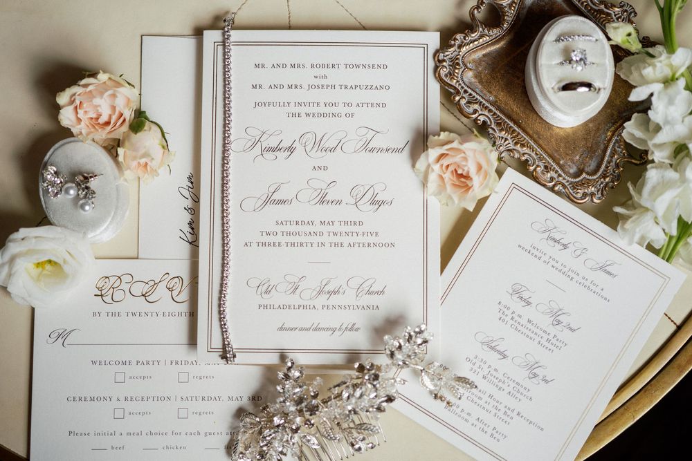 Elegant wedding invitation suite with blush roses and vintage frames laid flat on a cream-colored surface.