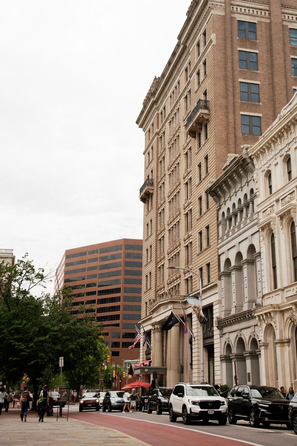 Historic downtown Portland architecture contrasts with modern buildings along a tree-lined street with parked cars and pedestrians.