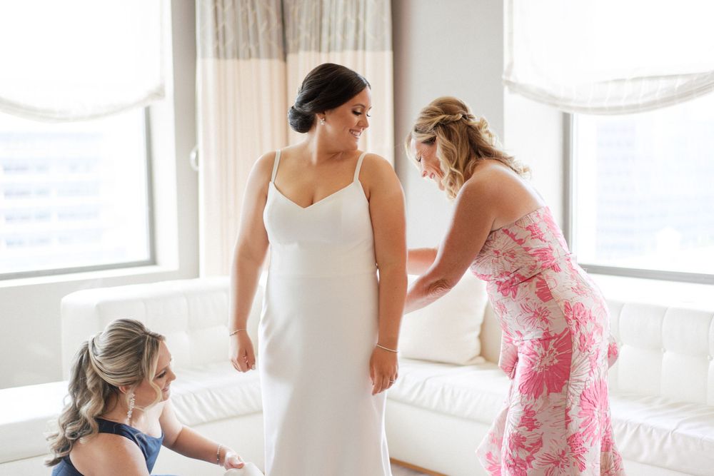 Three women in an elegant room prepare a bride in a white dress for her wedding ceremony.