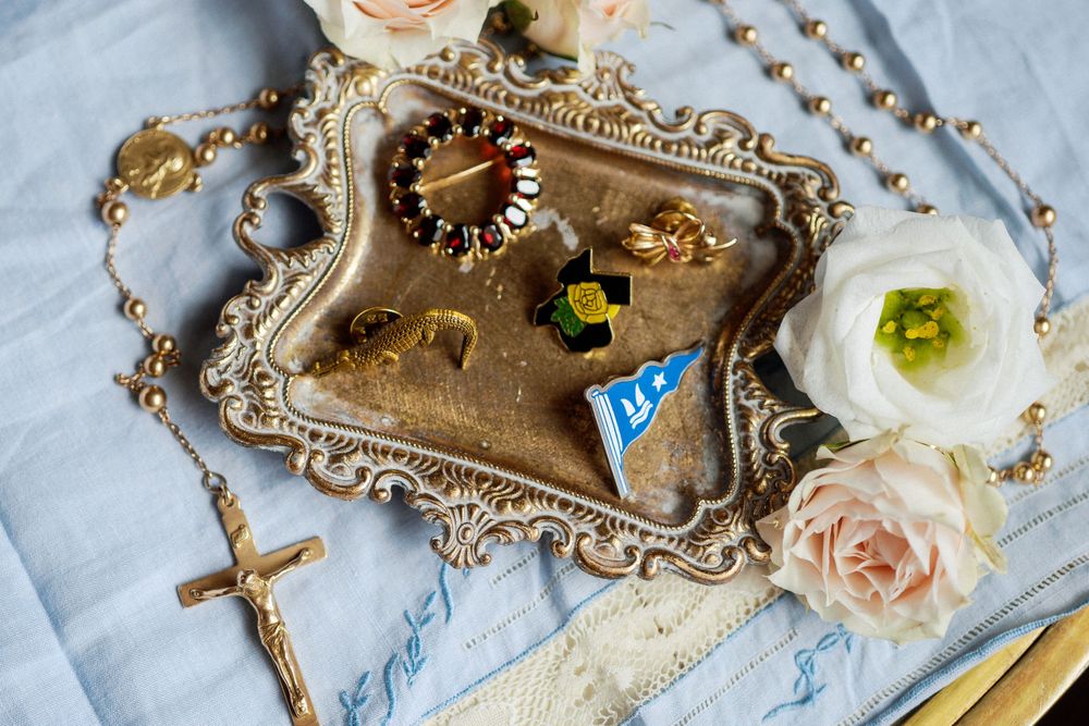 Vintage ornate gold tray with religious cross rosary beads and pink roses on light blue fabric background.