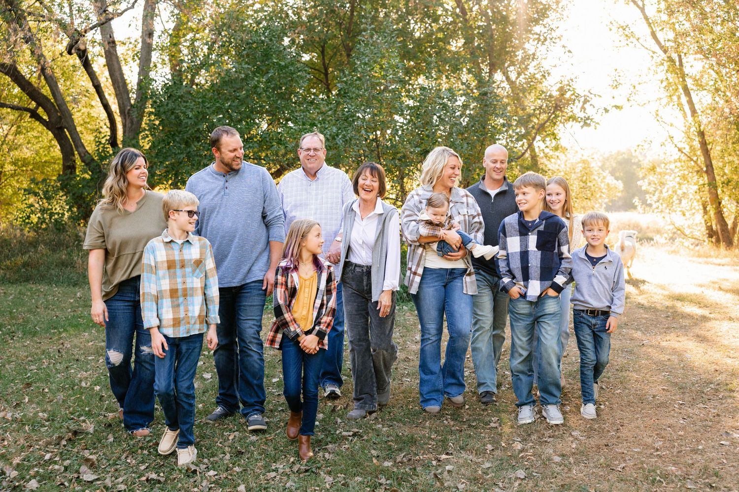 Large extended family group walking together on outdoor path in casual clothing during golden hour sunlit autumn setting.