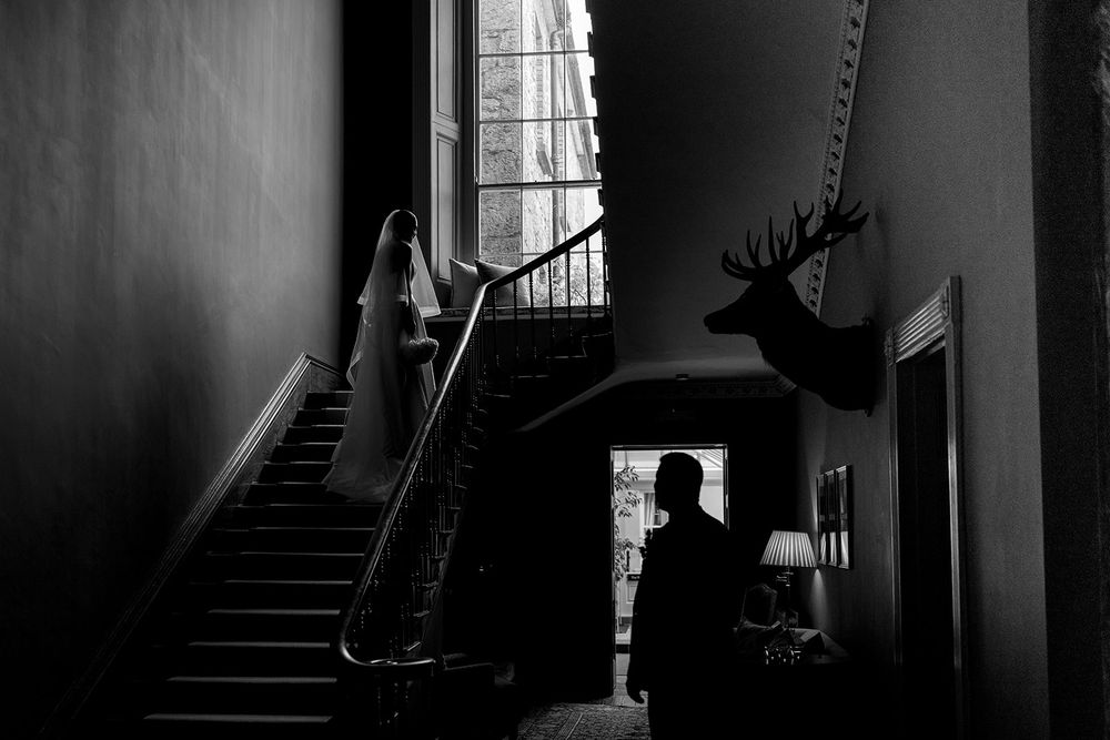 Dark moody interior with silhouette figure, staircase, and mounted deer head in dramatic black and white lighting.