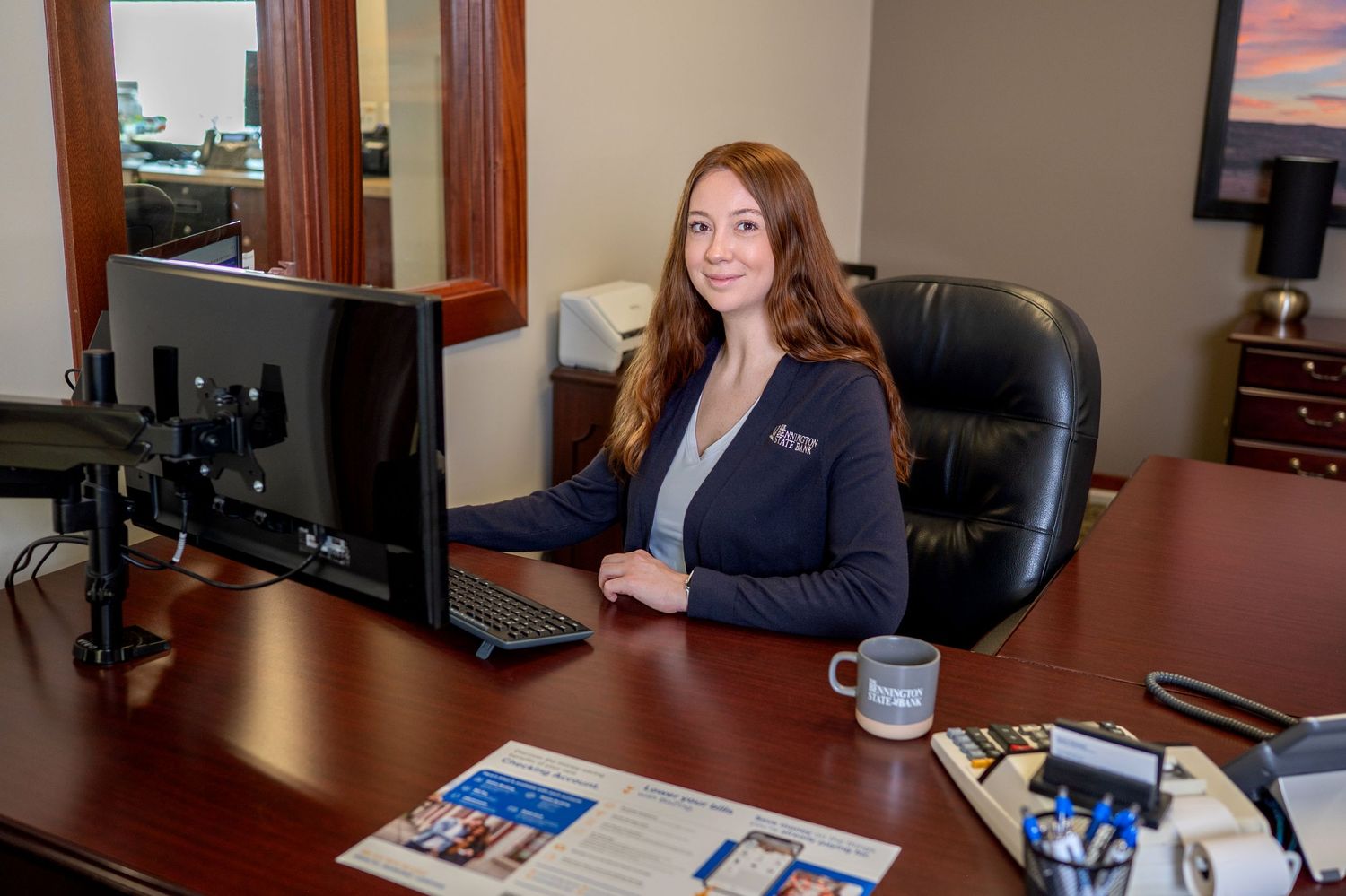 Two people having a business meeting in an office with a scenic sunset landscape displayed on a monitor behind them.