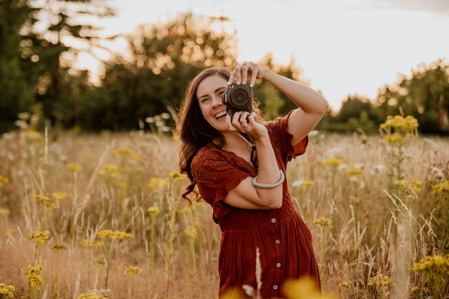 A photographer wearing a red dress takes pictures in a sunlit wildflower meadow at golden hour.