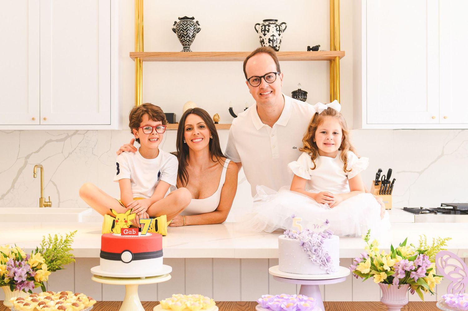 Family enjoying cake decorating together in bright modern kitchen with flowers and baked treats on counter.