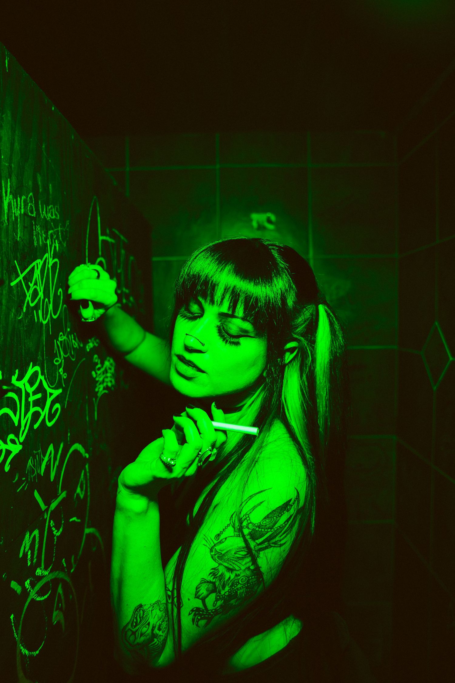 Moody nightclub scene bathed in neon green lighting showing silhouette posing against graffiti wall.