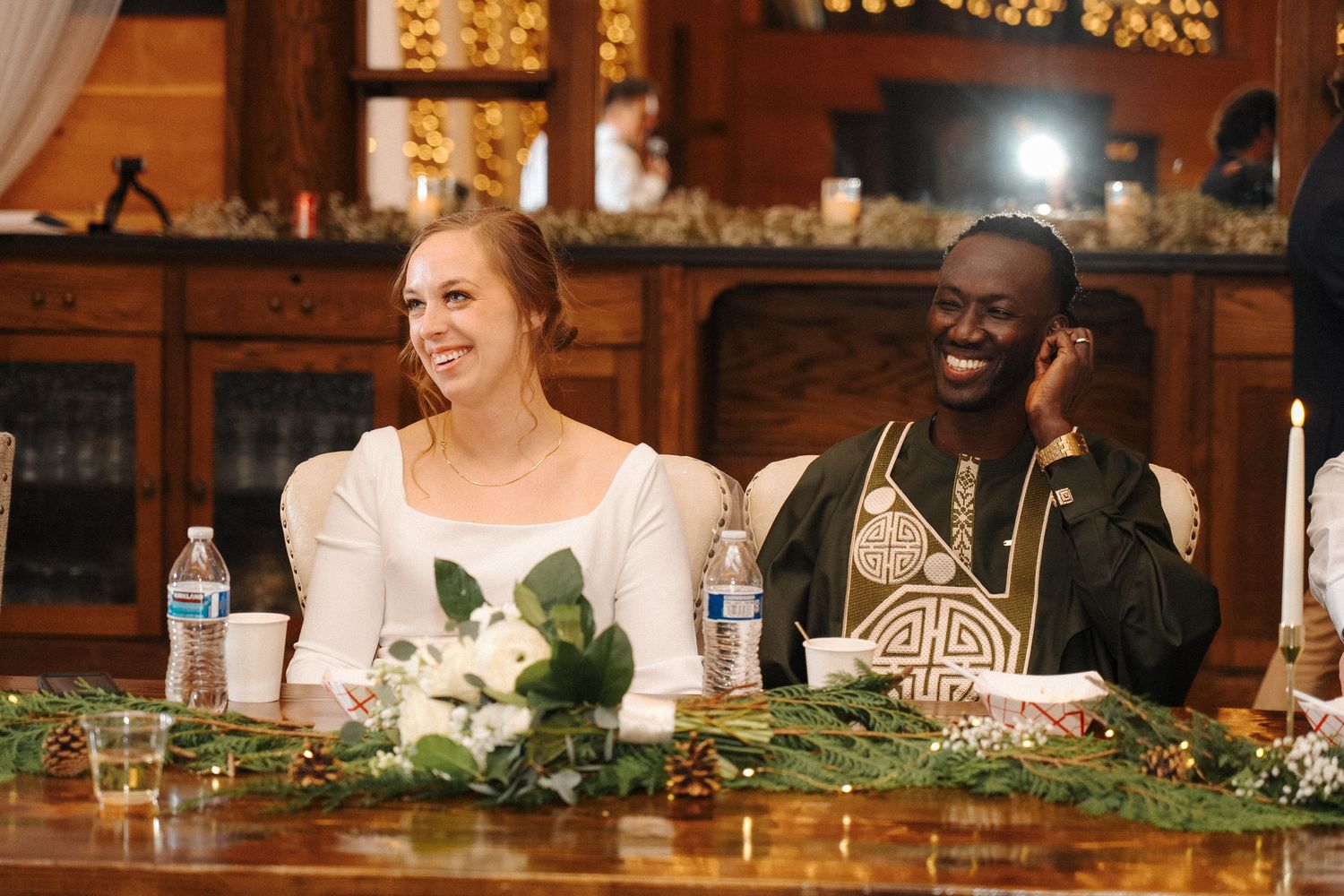 Happy couple shares a joyful moment at their reception table decorated with greenery and floral arrangements.