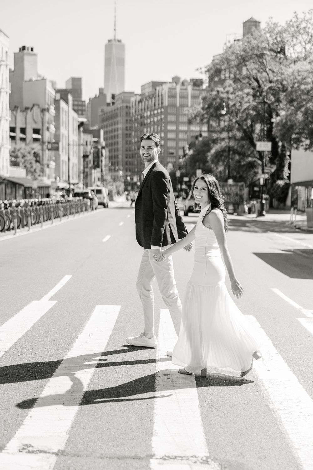 Black and white engagement photo with NYC skyline featuring couple on crosswalk in New York City.