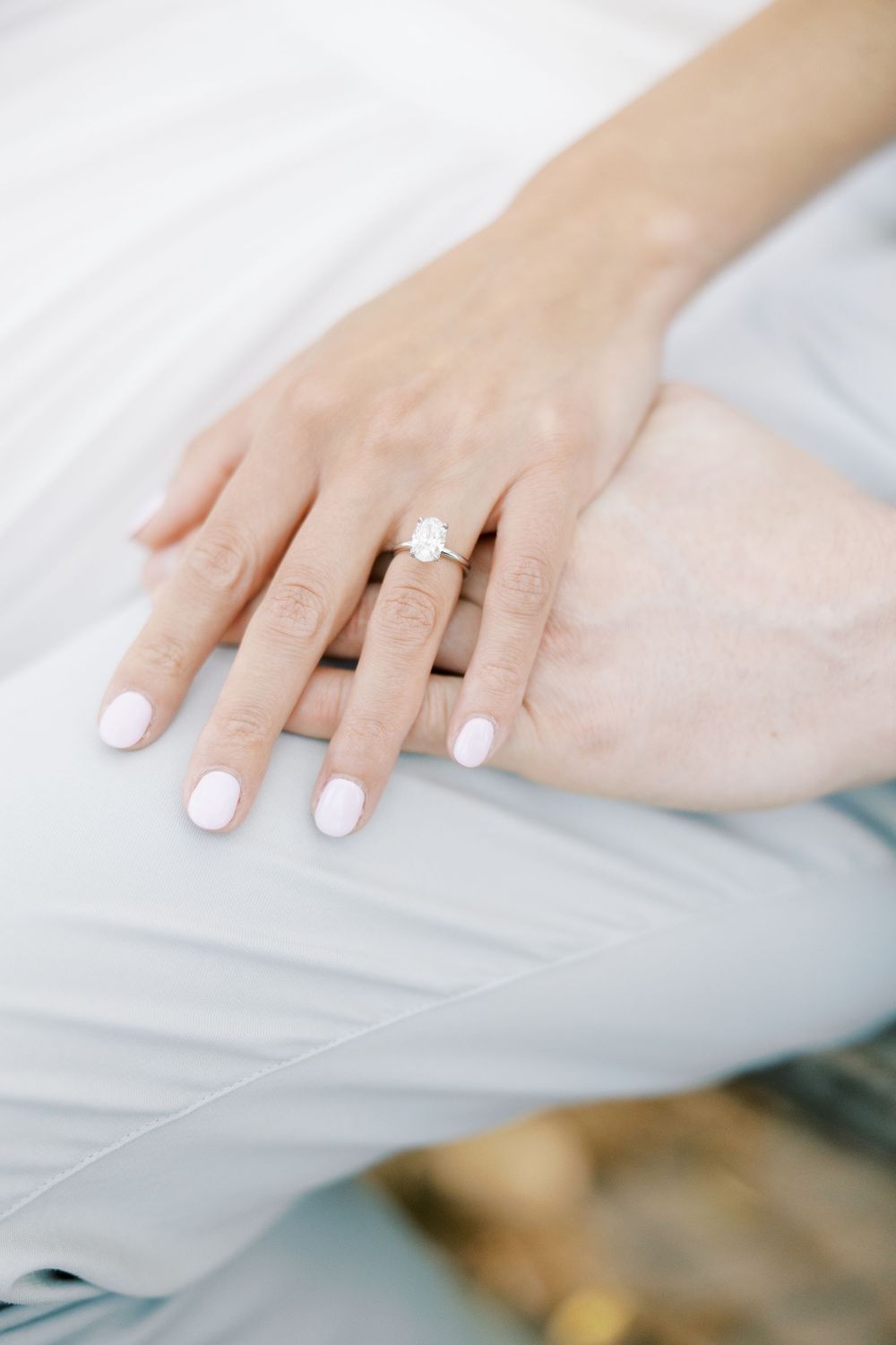 Close-up of a delicate hand wearing a sparkling engagement ring with white nail polish on a light background in New York City.