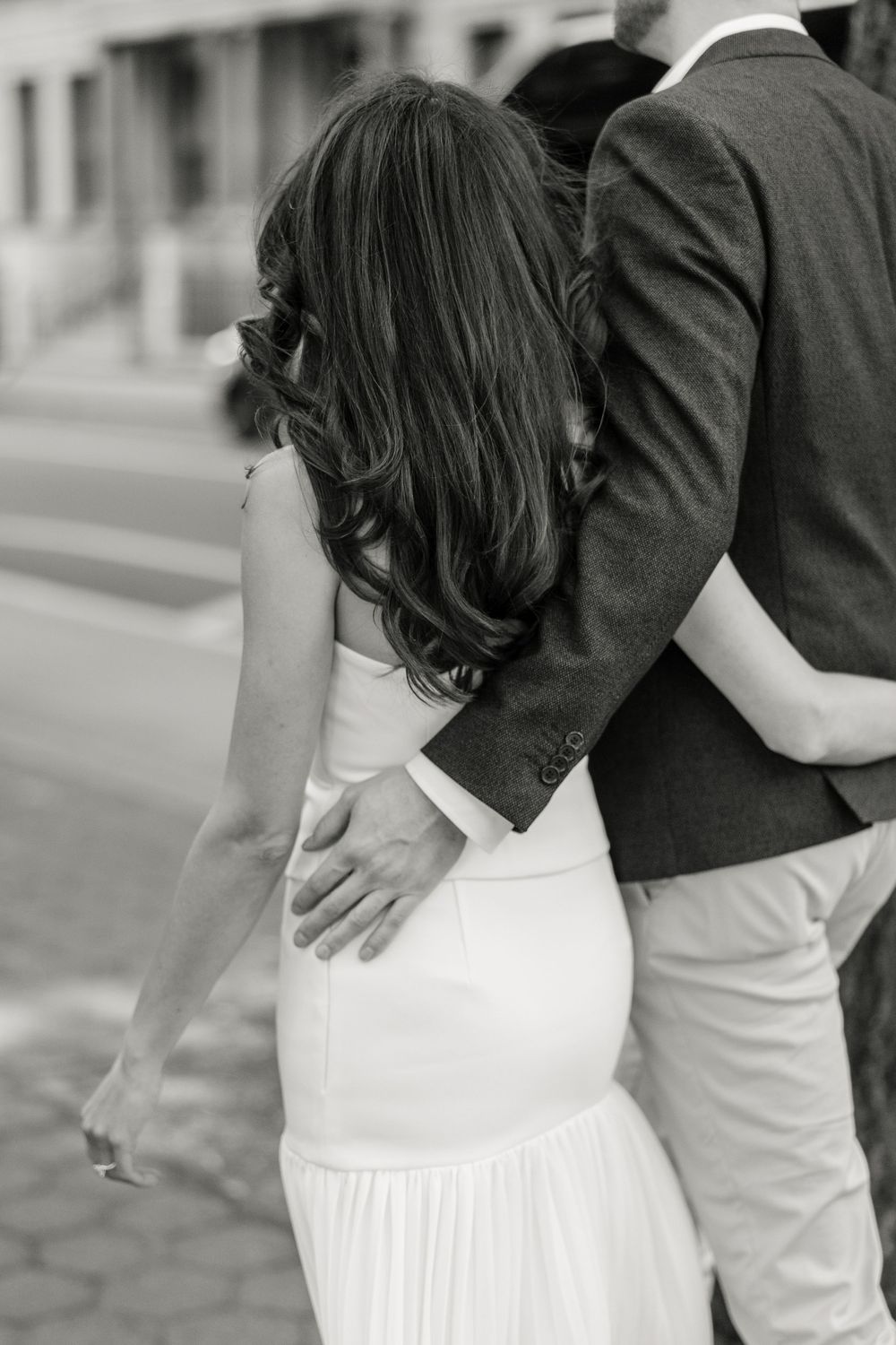 Back view of a couple in white and grey formal attire embracing on a city street in New York City.