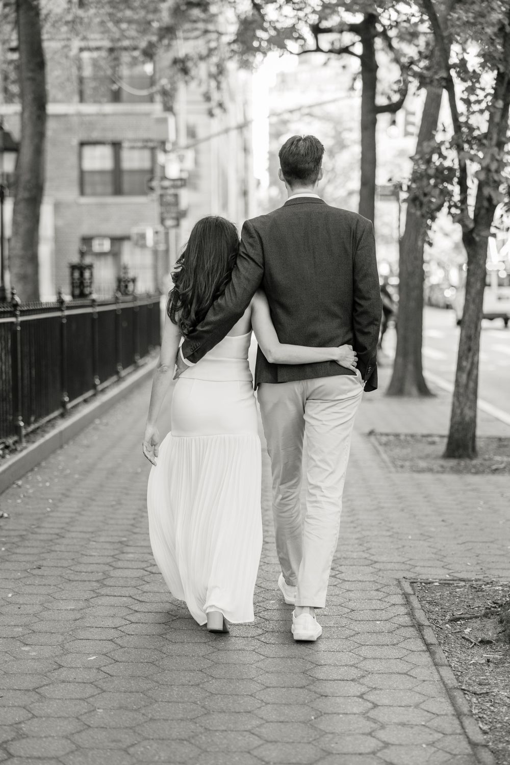 Black and white photo of a couple walking together on a cobblestone path in New York City.
