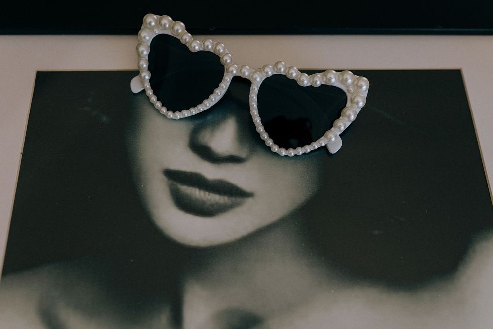 Black and white photo featuring sparkly heart-shaped sunglasses with rhinestone details against a shadowy backdrop.
