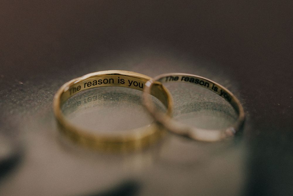 Two wedding rings with engraved messages inside positioned together on a blurred dark background.