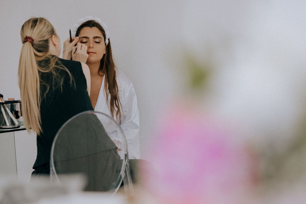 Professional hair styling session reflected in salon mirror with soft pink floral details in background.