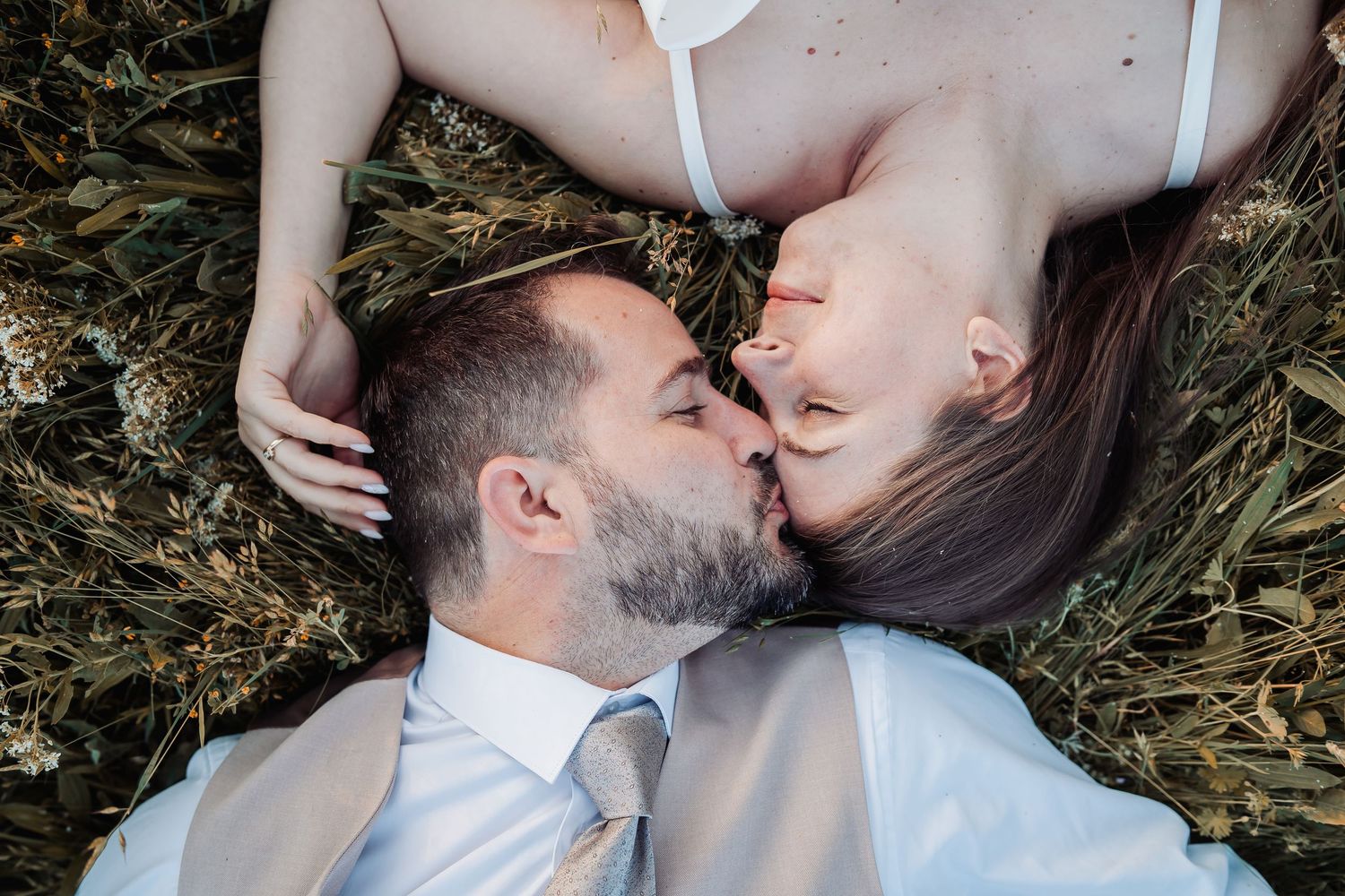 Two people lying in grass sharing an intimate moment in formal attire.