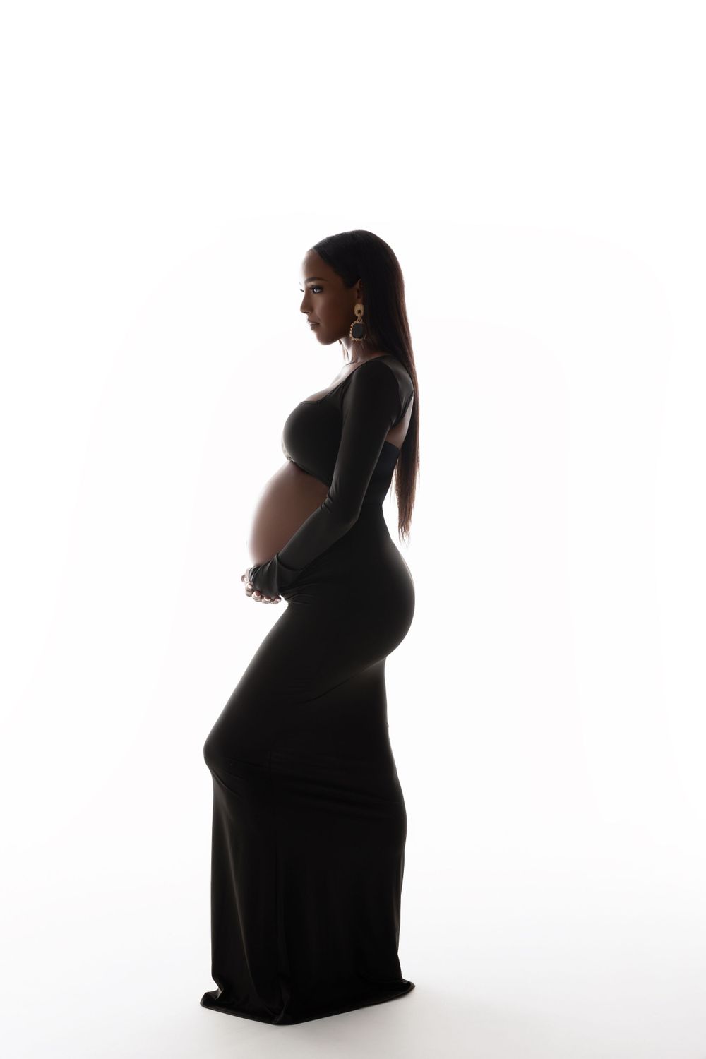 Artistic silhouette of a pregnant figure in a flowing black dress standing against a white background.