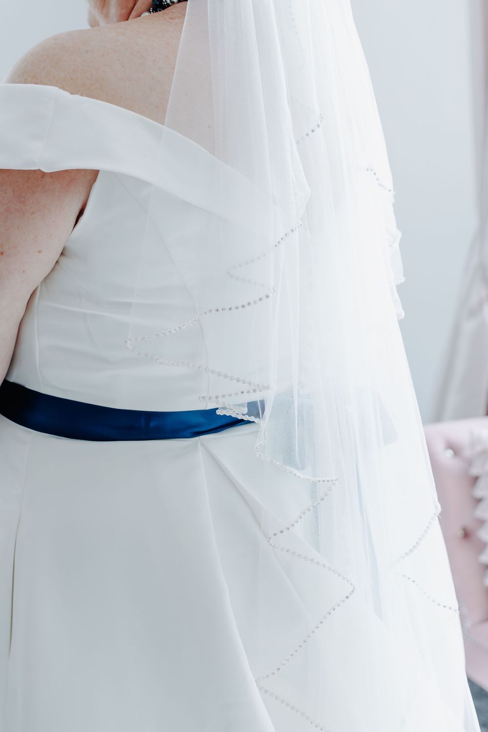 Close-up detail of a white wedding dress with flowing tulle fabric and a royal blue sash around the waist.