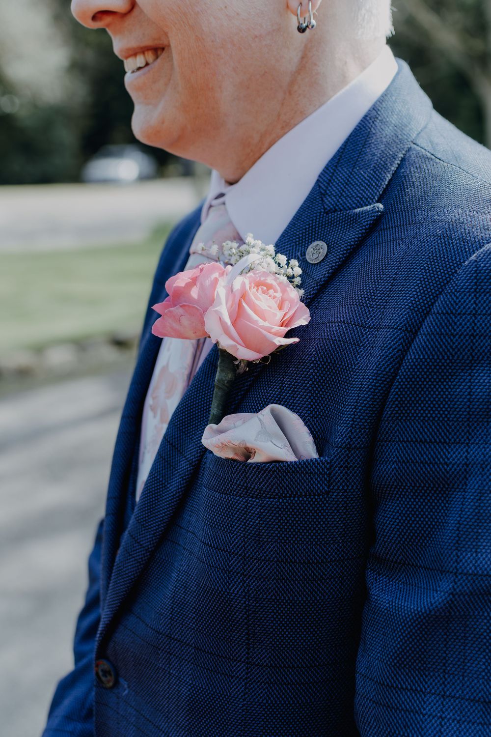 A wedding boutonniere with pink roses adorns a navy blue suit jacket with a light pocket square.