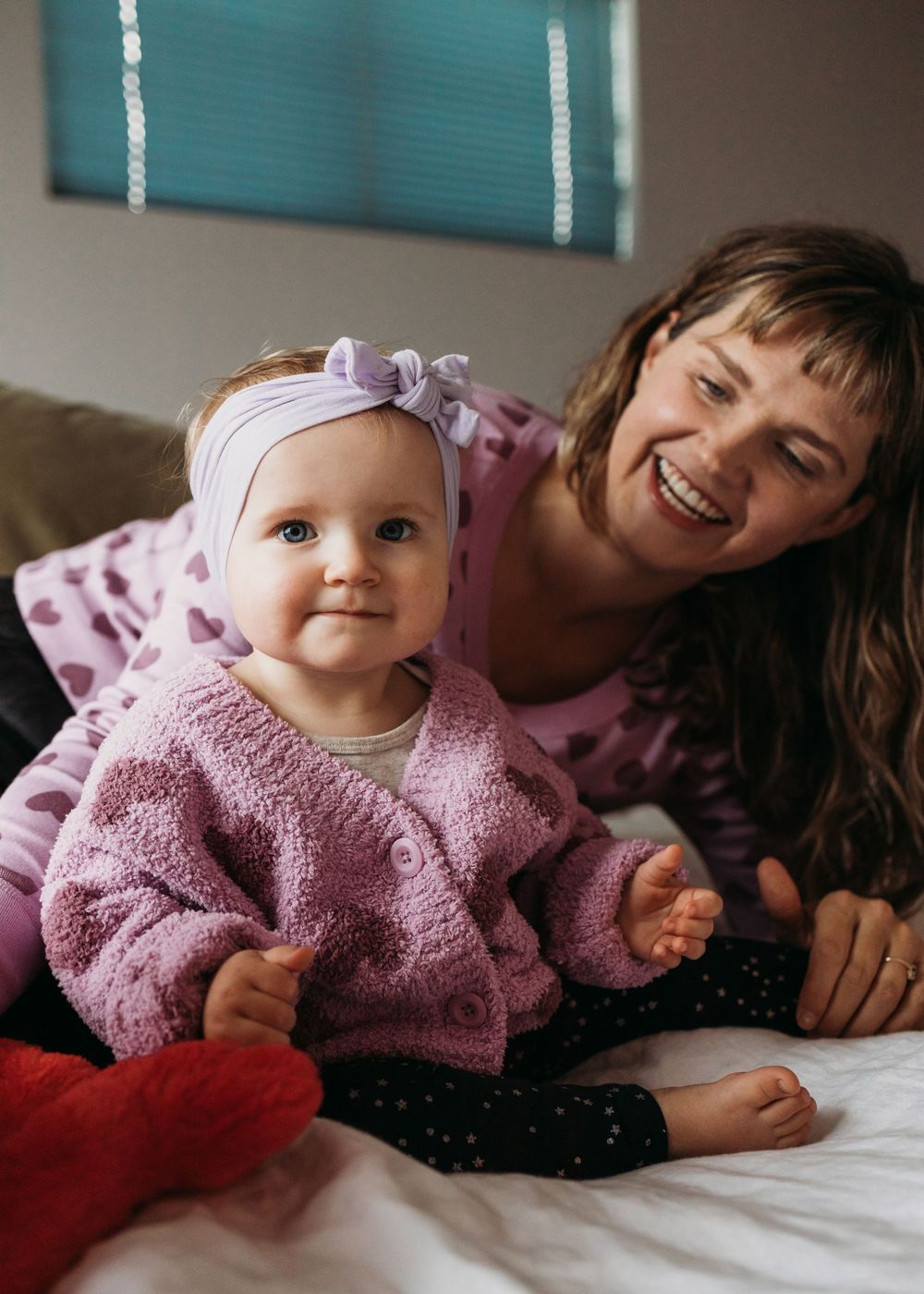 Candid moment of parent and small child in matching pink outfits relaxing on bed with joyful expressions.