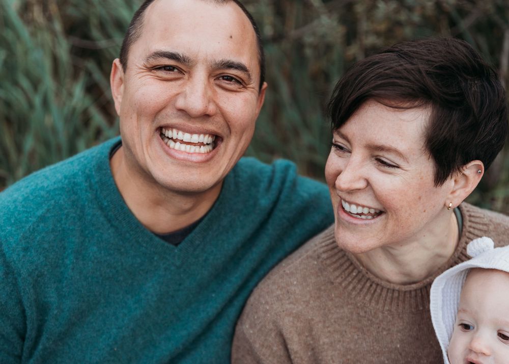 Two people wearing sweaters laugh joyfully together while sharing a candid moment during an outdoor photo session.